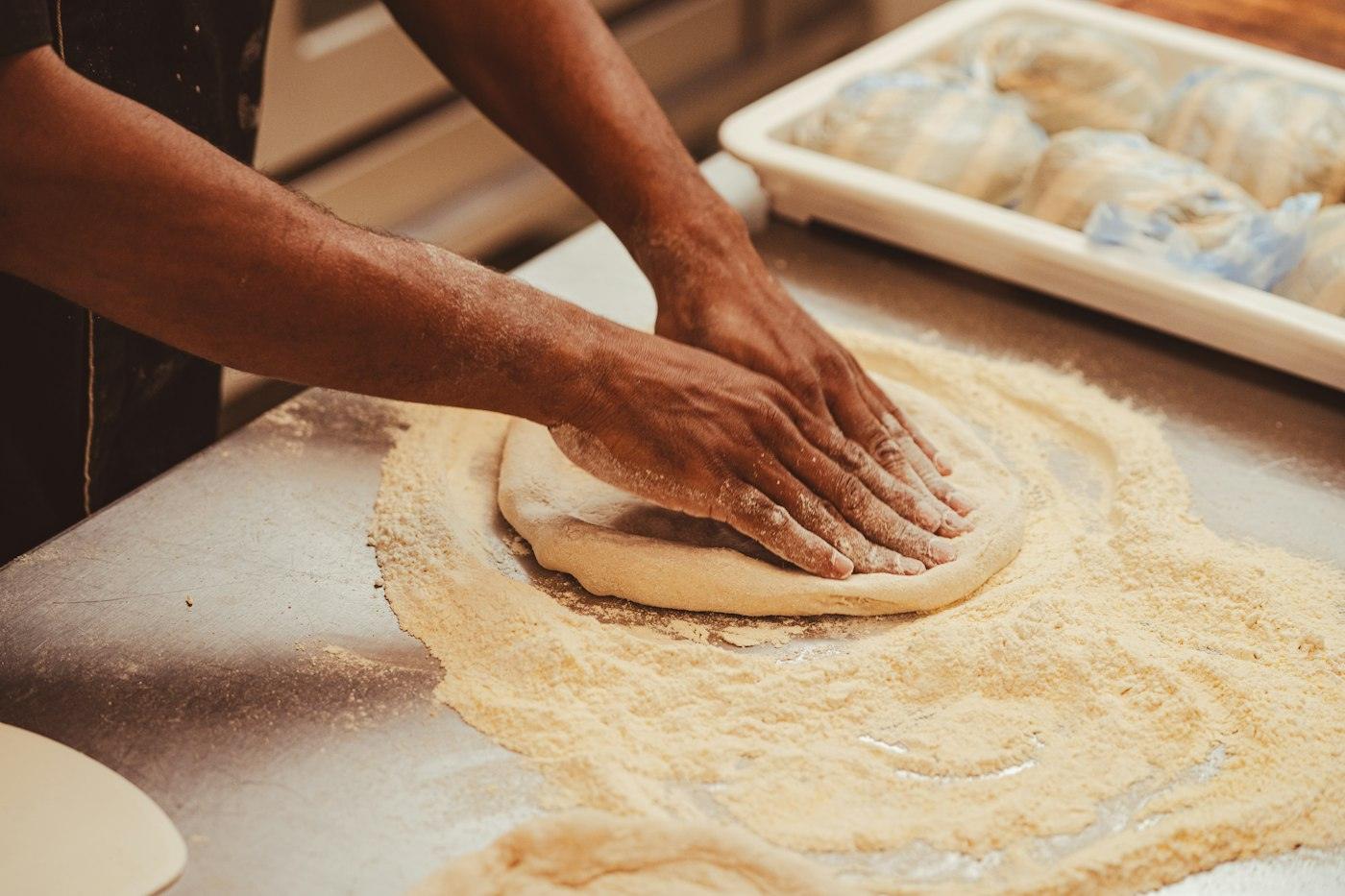 Mani che stendono l'impasto della pizza